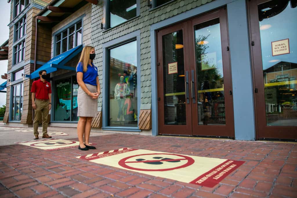 Guests wearing masks snap photos on social distancing markers outside a shuttered Disney Springs shop during the phased reopening.