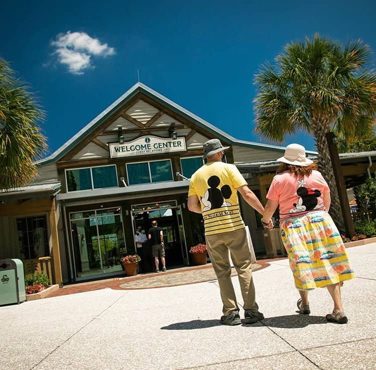 A joyful couple strolls hand-in-hand toward the Disney Springs Welcome Center, blue sky and palms setting the perfect photo scene.