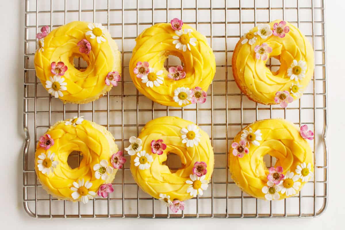 Six Rapunzel-inspired yellow donuts with pink and white flowers cool on a rack—perfect for a Disney park princess party treat.