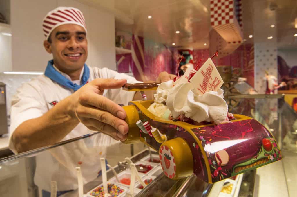 Cast member presents a whimsical ice cream sundae topped with whipped cream in a car dish, capturing Disney Cruise Line fun.