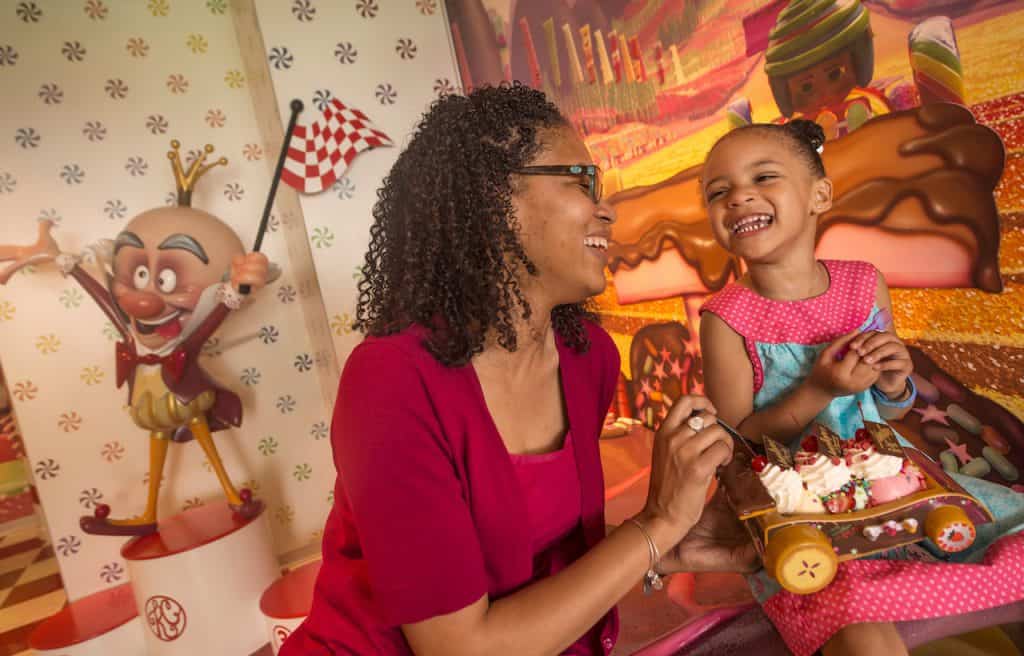 Guests aboard Disney Cruise Line enjoy a sweet moment, smiling with cupcakes in a vibrant, candy-inspired onboard setting.