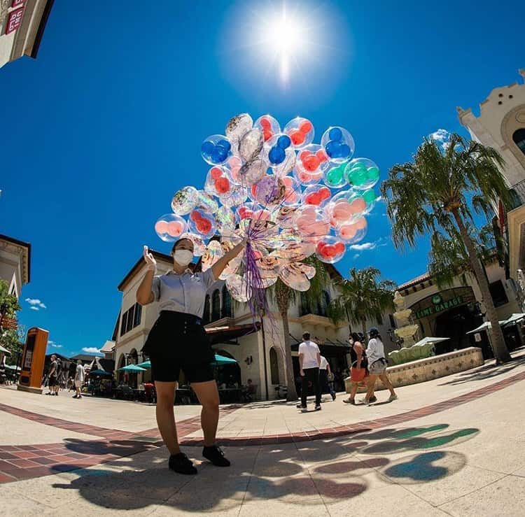 A Disney Springs guest carries vibrant balloons beneath palm trees, basking in the sunshine at this outdoor shopping destination.