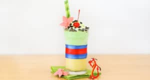 Mulan-themed milkshake in green and yellow layers, crowned with whipped cream, a cherry, and a Mulan dragon at Disney Parks.