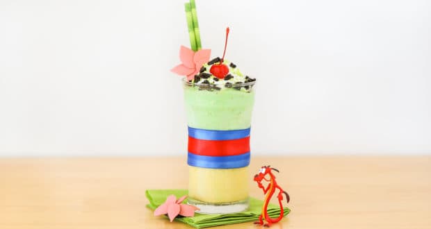 Mulan-themed milkshake in green and yellow layers, crowned with whipped cream, a cherry, and a Mulan dragon at Disney Parks.
