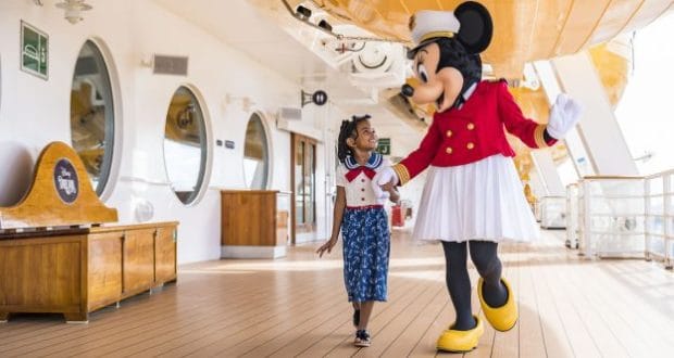 A smiling young girl holds hands with Minnie Mouse on the Disney Magic cruise deck, sharing magical moments on a Disney Cruise.