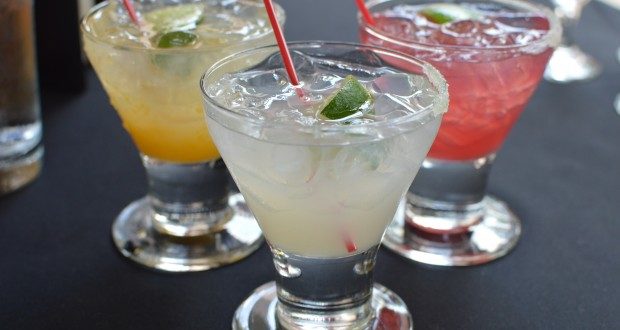 Three vibrant cocktails with lime wedges and straws on a dark table, recalling Florida’s bar ban for guests at Universal Orlando lounges.