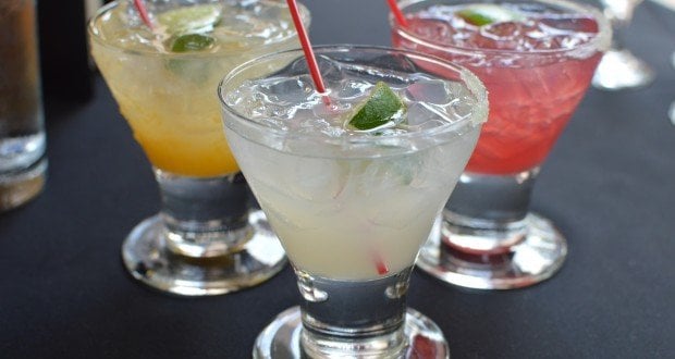 Three vibrant cocktails with lime wedges and straws on a dark table, recalling Florida’s bar ban for guests at Universal Orlando lounges.