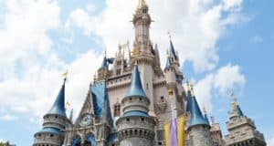Cinderella Castle rises majestically at Disney World with bright blue skies and fluffy clouds setting a perfect park day scene.