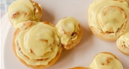 Mickey Mouse-shaped cinnamon rolls with yellow icing on a white plate, a magical Disney Parks-inspired treat for fans of all ages.
