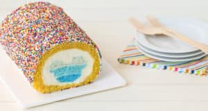 A sprinkle-covered cake roll with a Hidden Mickey-style blue and white heart inside, perfect for Disney fans, sits by party plates.