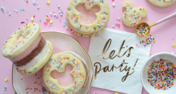 Magical Mickey-shaped ice cream sandwiches with sprinkles are ready to party on a pink table beside a festive "let's party!" napkin—Disney treat style.