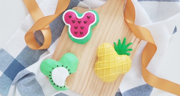 Vibrant fruit-shaped cookies (watermelon, kiwi, pineapple) on a board evoke a festive Disney park summer picnic treat.