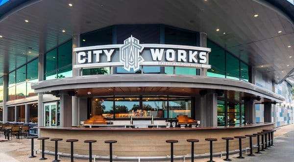 City Works Eatery at Disney Springs, sporting its bold sign, lively outdoor bar, and sleek glass facade after reopening.