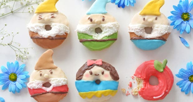 Snow White and three dwarf donuts, plus a bitten apple, displayed with blue flowers—magical treats fit for a Disney Parks celebration.