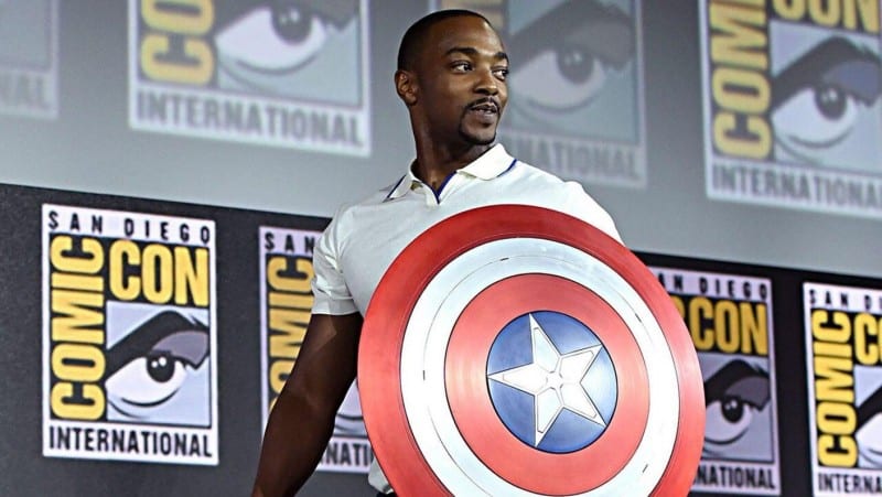 Falcon rocks Captain America's shield at San Diego Comic-Con, posing heroically before iconic Comic-Con International signage.