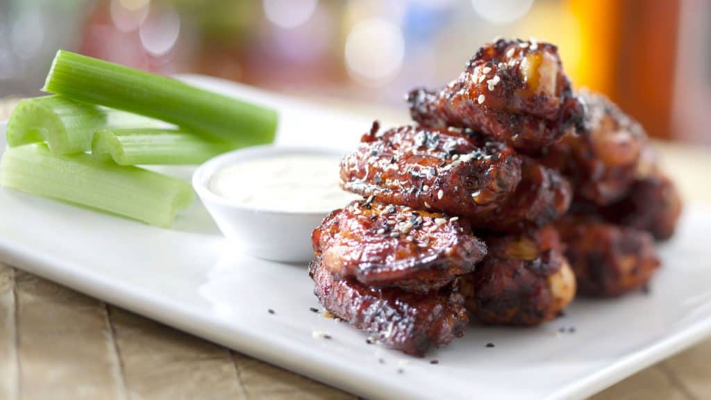 Ohana-style barbecue wings with sesame seeds, celery, and dip, just like at Disney’s Polynesian Village Resort, on a white plate.