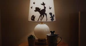 A Bambi-inspired table lamp with animal silhouettes glows beside a plant and mug, perfect for Disney fans’ cozy spaces.