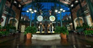 Port Orleans Resort – French Quarter’s elegant atrium features a central fountain, lush greenery, and glowing glass ceiling at sunset.