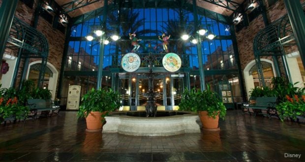 Port Orleans Resort – French Quarter’s elegant atrium features a central fountain, lush greenery, and glowing glass ceiling at sunset.