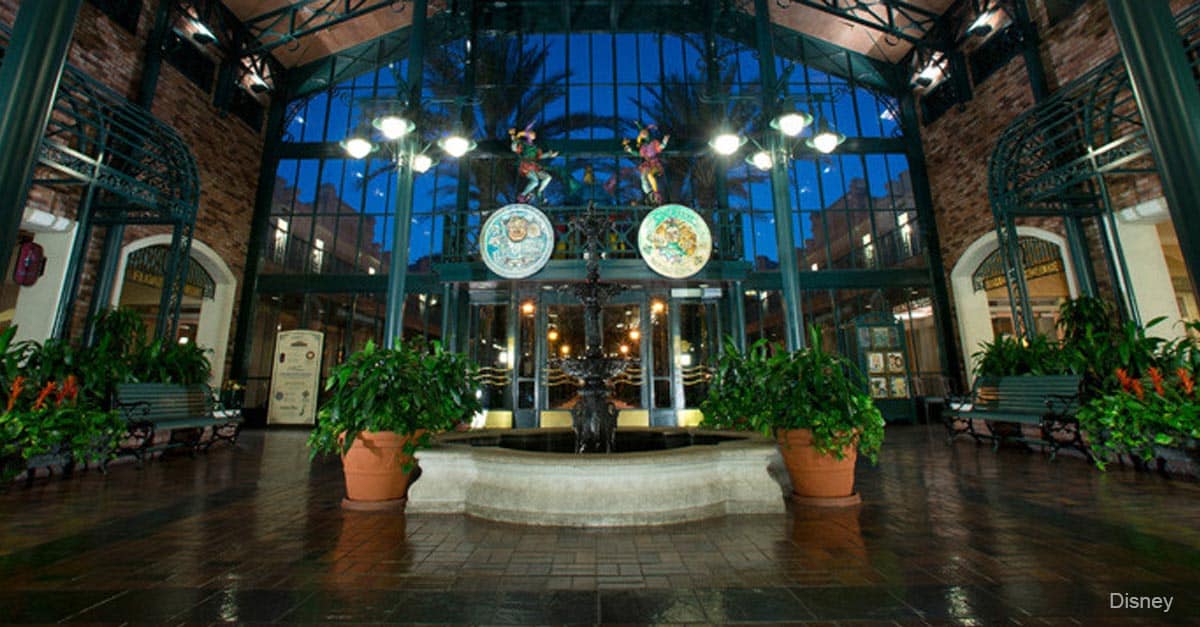 Port Orleans Resort – French Quarter’s elegant atrium features a central fountain, lush greenery, and glowing glass ceiling at sunset.