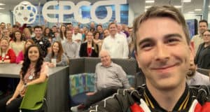 Zach Riddley joins a group of Disney fans for a selfie in an EPCOT office, with the iconic EPCOT sign glowing behind them.