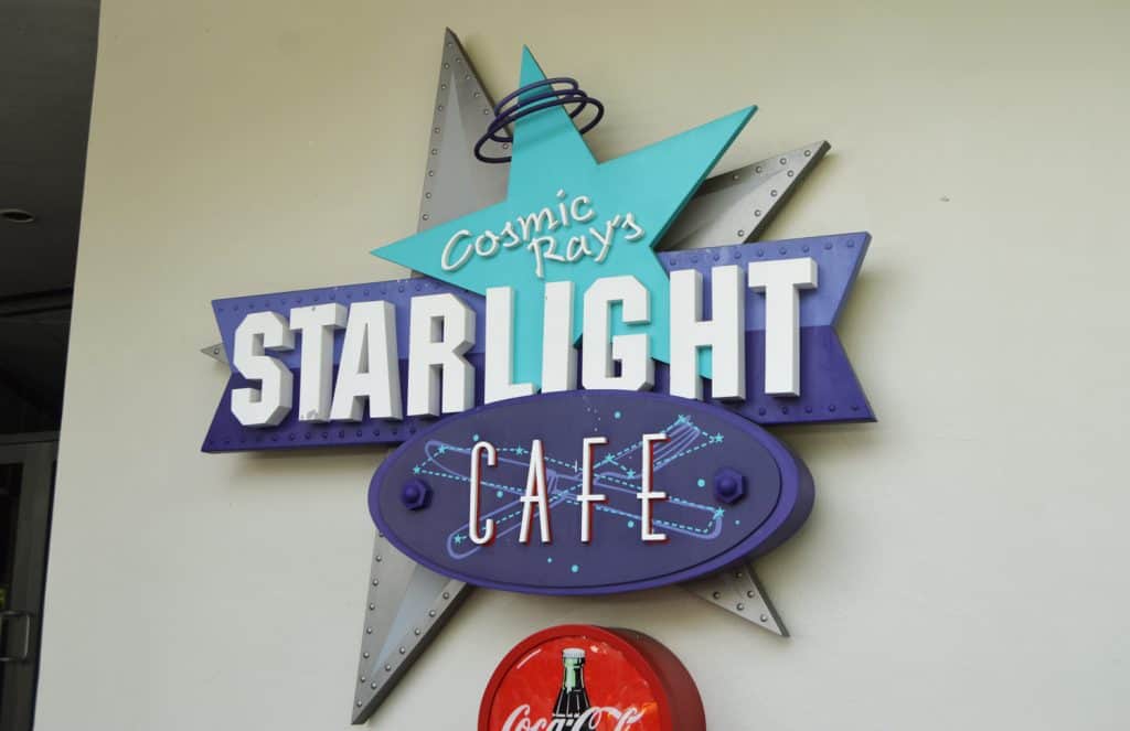 Cosmic Ray’s Starlight Café sign with starry, space-themed graphics stands out on a white wall at Magic Kingdom.