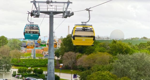 Disney Skyliner gondolas soar above lush trees on a cloudy day, treating park guests to enchanting aerial Disney World views.