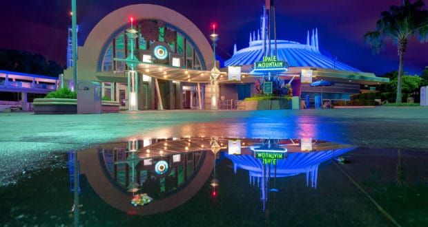 Space Mountain glows in neon at night, its reflection shimmering in a puddle—a Magic Kingdom highlight for Disney fans.