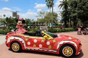 Minnie Mouse waves from a red, polka-dot convertible adorned with flowers, capturing the enchantment of Disney World.