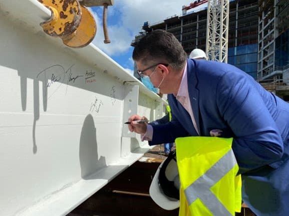A Disney executive in a suit signs a steel beam at the Swan & Dolphin expansion site, hard hat and vest in hand at Disney World.