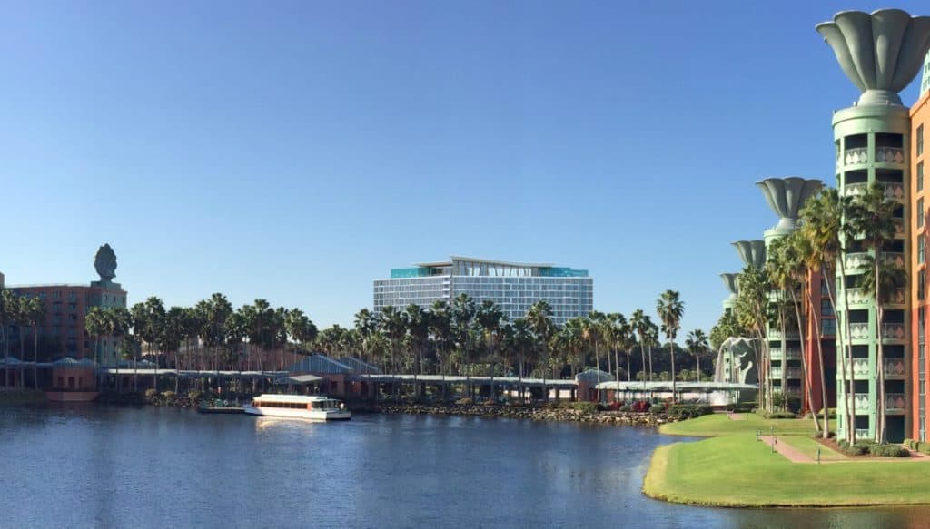 A Friendship Boat cruises the lake by palm trees and the iconic Walt Disney World Swan and Dolphin Resort under a bright blue sky.