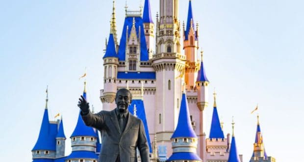 Walt Disney and Mickey Mouse statue stands before Cinderella Castle at Disney World, framed by vibrant pink flowers in bloom.