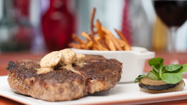 Grilled steak topped with herb butter, crispy fries, and greens—fan-favorite dish steps from Crescent Lake at Disney World.