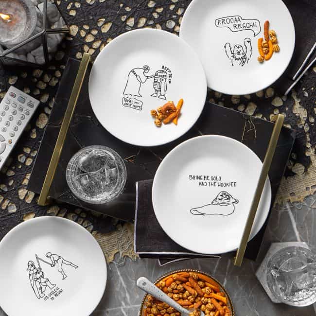 Corelle Collection Star Wars plates display fan-favorite characters and themed snacks atop a dark table, with festive drinks, crunchy nuts, and a TV remote nearby—perfect for an out-of-this-galaxy movie marathon just like at Disney’s Star Wars: Galaxy’s Edge.