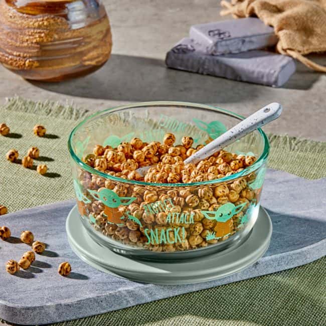 Star Wars Corelle Collection glass bowl featuring colorful cartoon designs and the phrase "snack attack," filled with cereal and a spoon—perfect for fans enjoying a themed breakfast inspired by the Force at Galaxy's Edge.