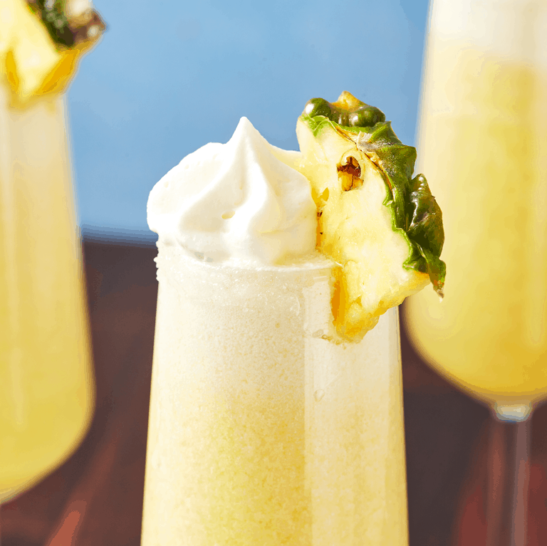 Dole Whip-inspired yellow frozen treat served in a glass, crowned with whipped cream and finished with a pineapple slice, just like the iconic refreshment found at Disney parks.