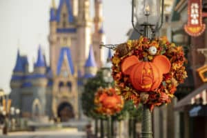 A Mickey Mouse-shaped pumpkin wreath decorated with autumn leaves hangs on a lamppost; Cinderella Castle is blurred in the background, creating a festive Halloween scene at a Disney park.