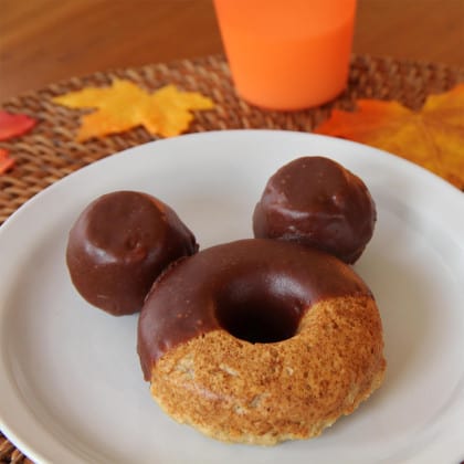 Chocolate-glazed donut and two donut holes form Mickey Mouse ears on a plate—just like a Disney Parks treat!.