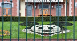 Mickey Mouse’s iconic face, crafted from vibrant flowers, greets fans at the gates of Disneyland, seen through the park’s ornate metal fence as guests eagerly anticipate news of California theme parks reopening.