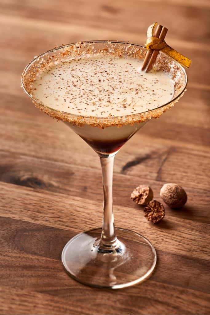 A festive, creamy cocktail in a martini glass with a spiced rim is dressed up with cinnamon and nutmeg on top, ready to be enjoyed at Disney Springs—perfect for guests seeking a magical Fall Specialty Cocktail during their visit.