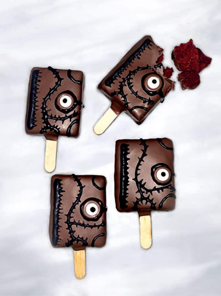 Enjoy four Hocus Pocus-inspired monster chocolate popsicles, each with candy eyes and stitched designs, including one with a playful bite missing. These spooky treats are perfect for Halloween celebrations at the park or to pre-order alongside our Spell Book Cake Pops for your next themed party.