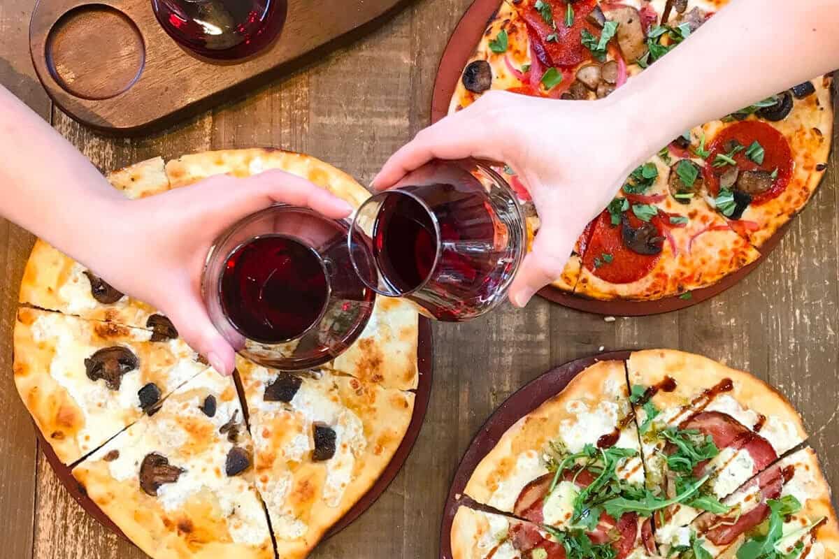 Friends toast glasses of red wine over gourmet pizzas at a Disney Springs hotspot, capturing the festive Disney vibes.