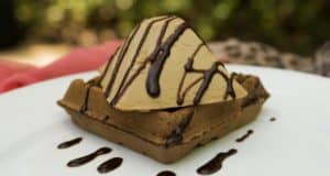 A Disney-inspired pyramid ice cream atop a Mickey waffle, drizzled with chocolate, served on a white plate—magical treat!.