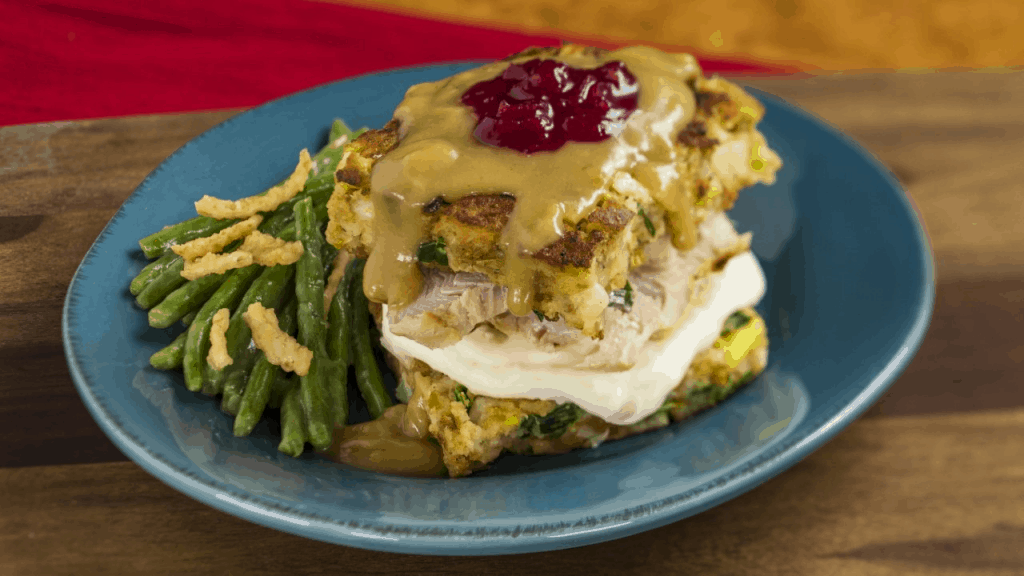 A festive blue plate at the EPCOT International Festival of the Holidays featuring sliced turkey, stuffing, green beans, creamy gravy, and a dollop of cranberry sauce—a classic holiday favorite available starting November 27 for theme park foodies.