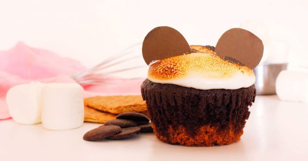 Chocolate cupcake topped with toasted marshmallow and Mickey Mouse chocolate ears, served alongside classic Disney park treats.