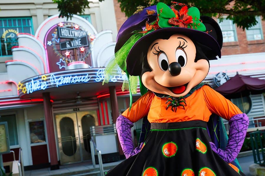 Minnie Mouse, dressed as a whimsical witch, greets guests outside the glowing neon lights of Hollywood & Vine at Disney’s Hollywood Studios. The restaurant shines with festive energy, inviting everyone to join Minnie’s Halloween Dine and soak up the enchanting Halloween atmosphere.