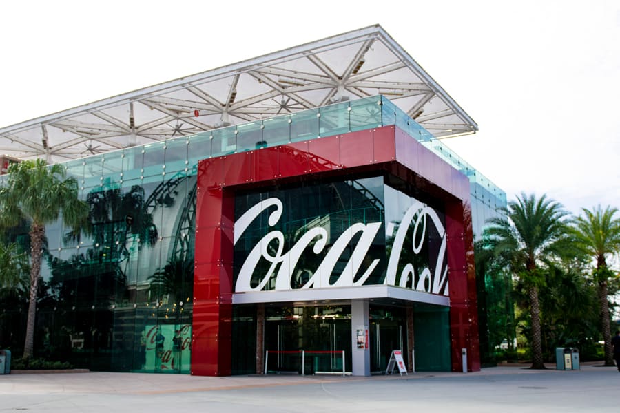 The sleek, modern Coca-Cola building with its iconic logo stands out among palm trees and the sunny skies of Disney Springs at Walt Disney World Resort, inviting guests to experience a world of refreshing flavors and interactive fun.