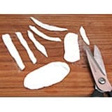 Scissors and pieces of white paper shaped for magical crafting sit on a wooden table, ready to create Mickey Mummy Cupcake toppers inspired by the Halloween festivities at Disney Parks.