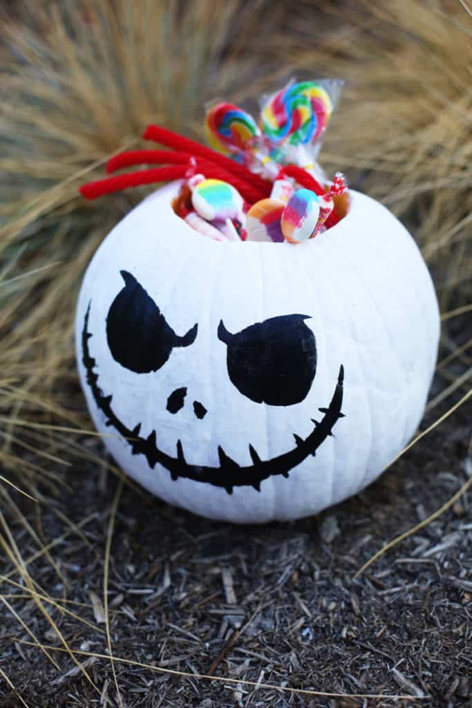 Jack Skellington-inspired white no-carve pumpkin candy holder, brimming with vibrant lollipops, displayed in a garden setting—an enchanting Disney Halloween centerpiece perfect for bringing the spirit of Haunted Mansion Holidays or Mickey’s Not-So-Scary Halloween Party to your celebration.