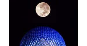 A glowing full moon rises above Epcot’s iconic blue geodesic dome, Spaceship Earth, casting an enchanting and slightly spooky light over the park’s night skyline, evoking the magic of a Disney adventure after dark.